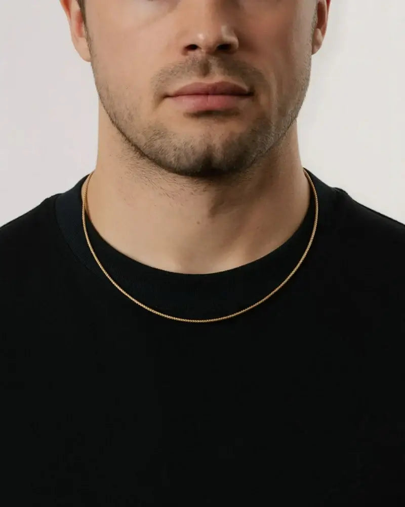 Gouden box ketting gedragen door man met een zwart t-shirt.
