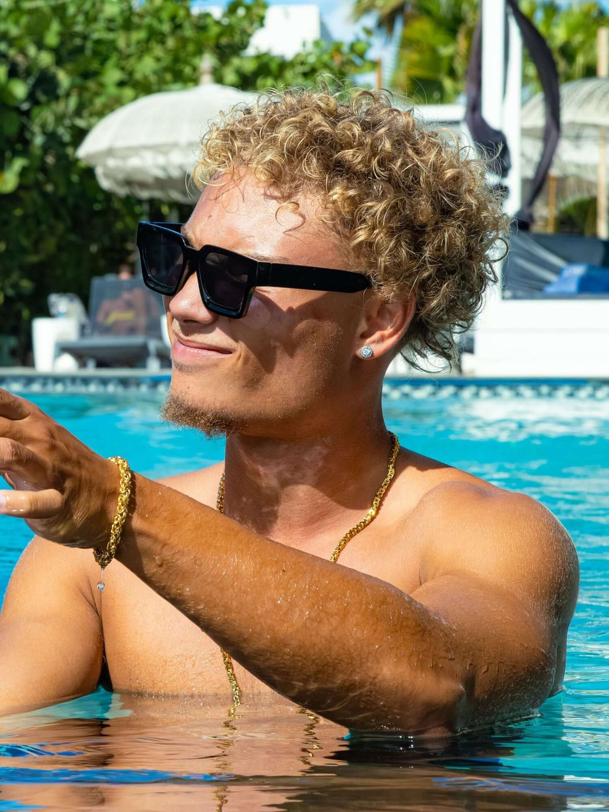 Man met oorknopjes en een goudkleurige ketting en armband in een zwembad