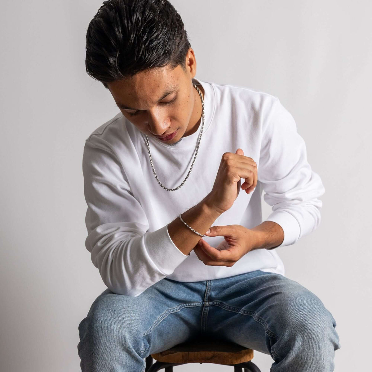 Jongeman in witte trui en jeans, siert zijn pols met Roestvrij Staal (RVS) Sieraden.