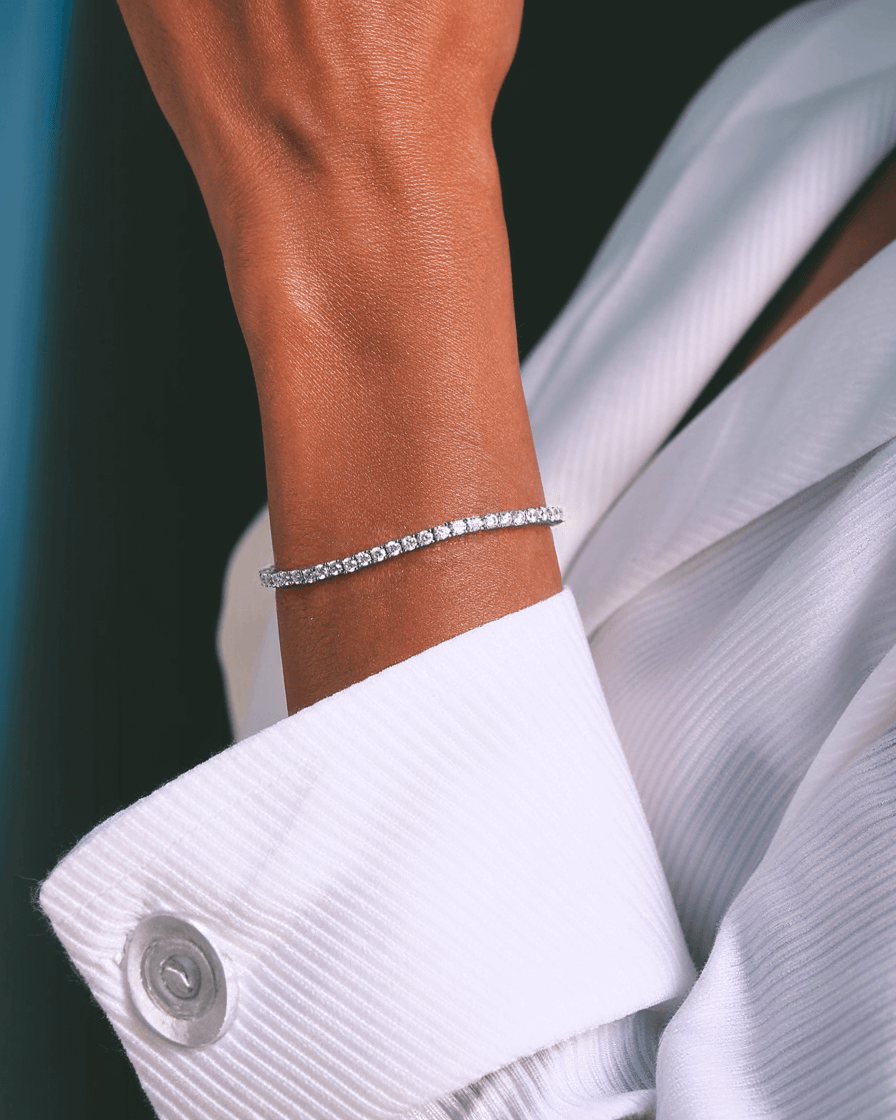 Close-up van een vrouwelijk model met een elegante zilveren tennis armband met zirkonia stenen om de pols, gestyled met een witte blouse. Luxe sieraden voor dames, perfect als verfijnde en tijdloze accessoire.