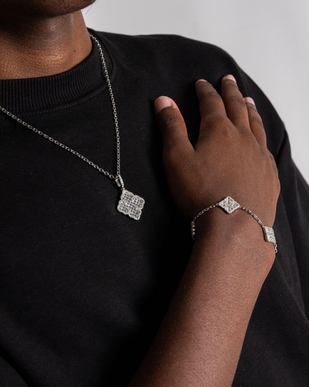 Clover hanger zilver worn as a necklace and bracelet with sparkling stones on a model's wrist and neck.