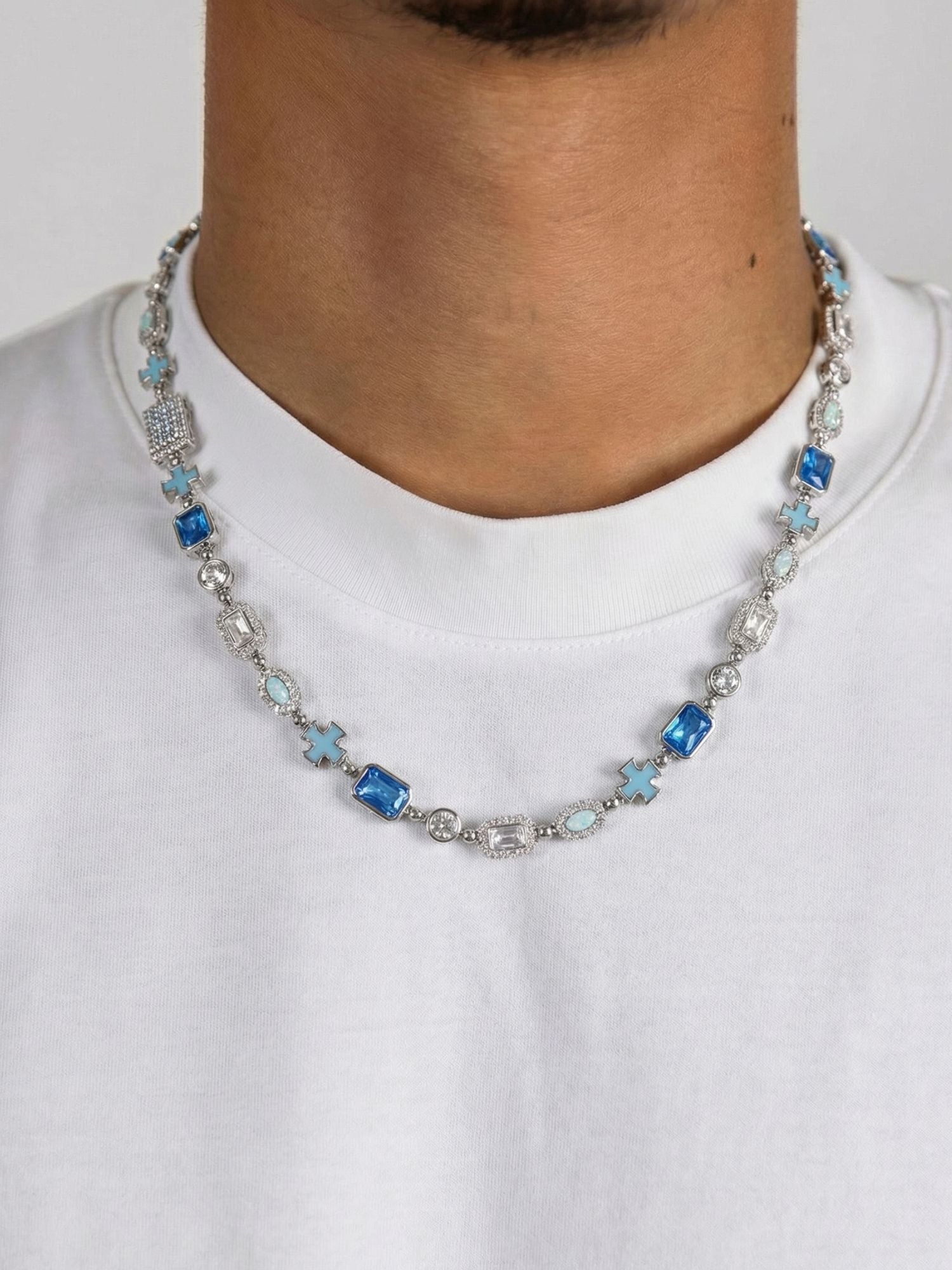 Kruis en Blauwe Edelstenen Ketting ICE Witgoud gedragen door een model in een witte shirt.