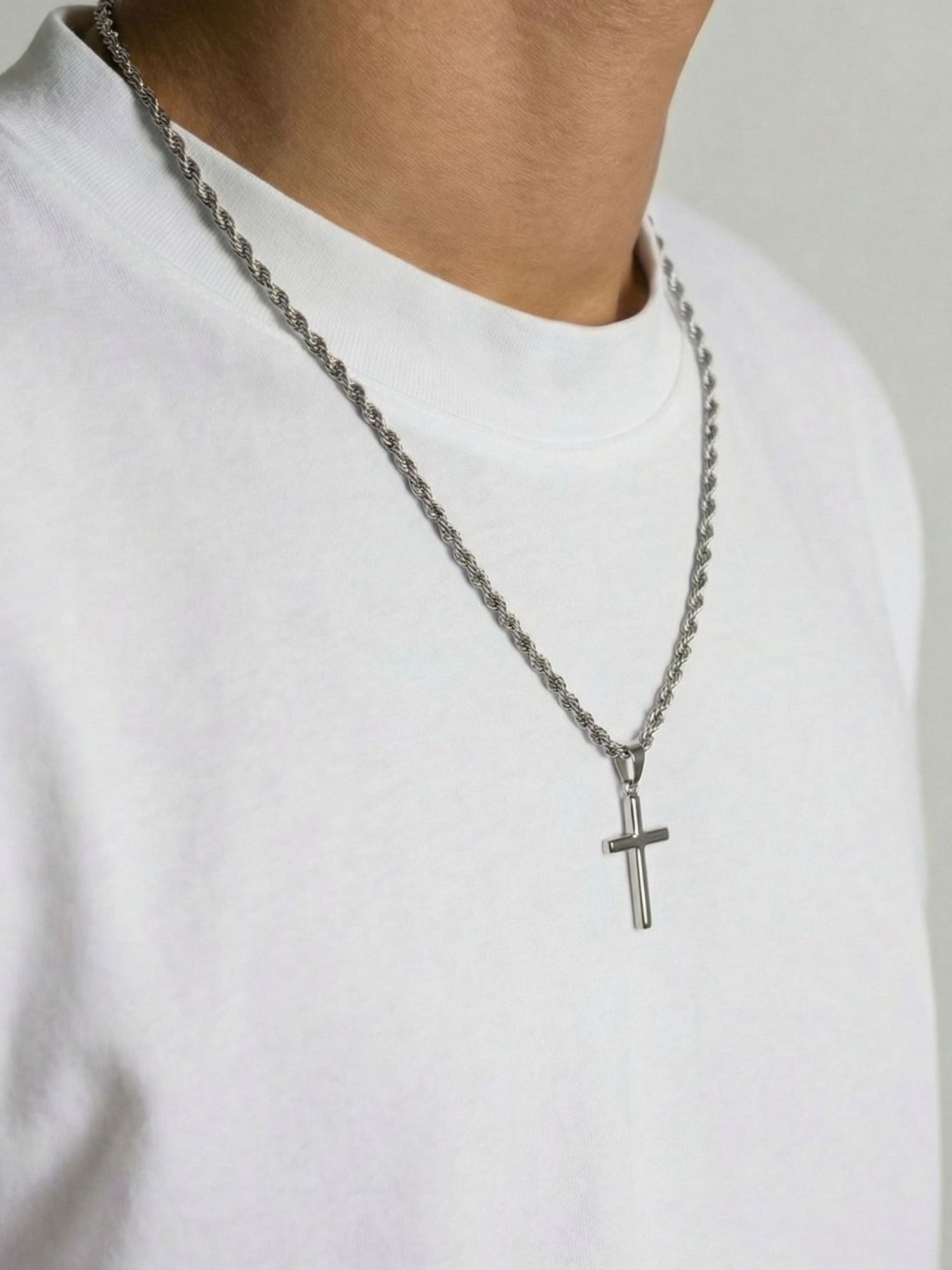 Zilveren kruis hanger draagt een man, zichtbaar op een zilverkleurige ketting met een moderne uitstraling.