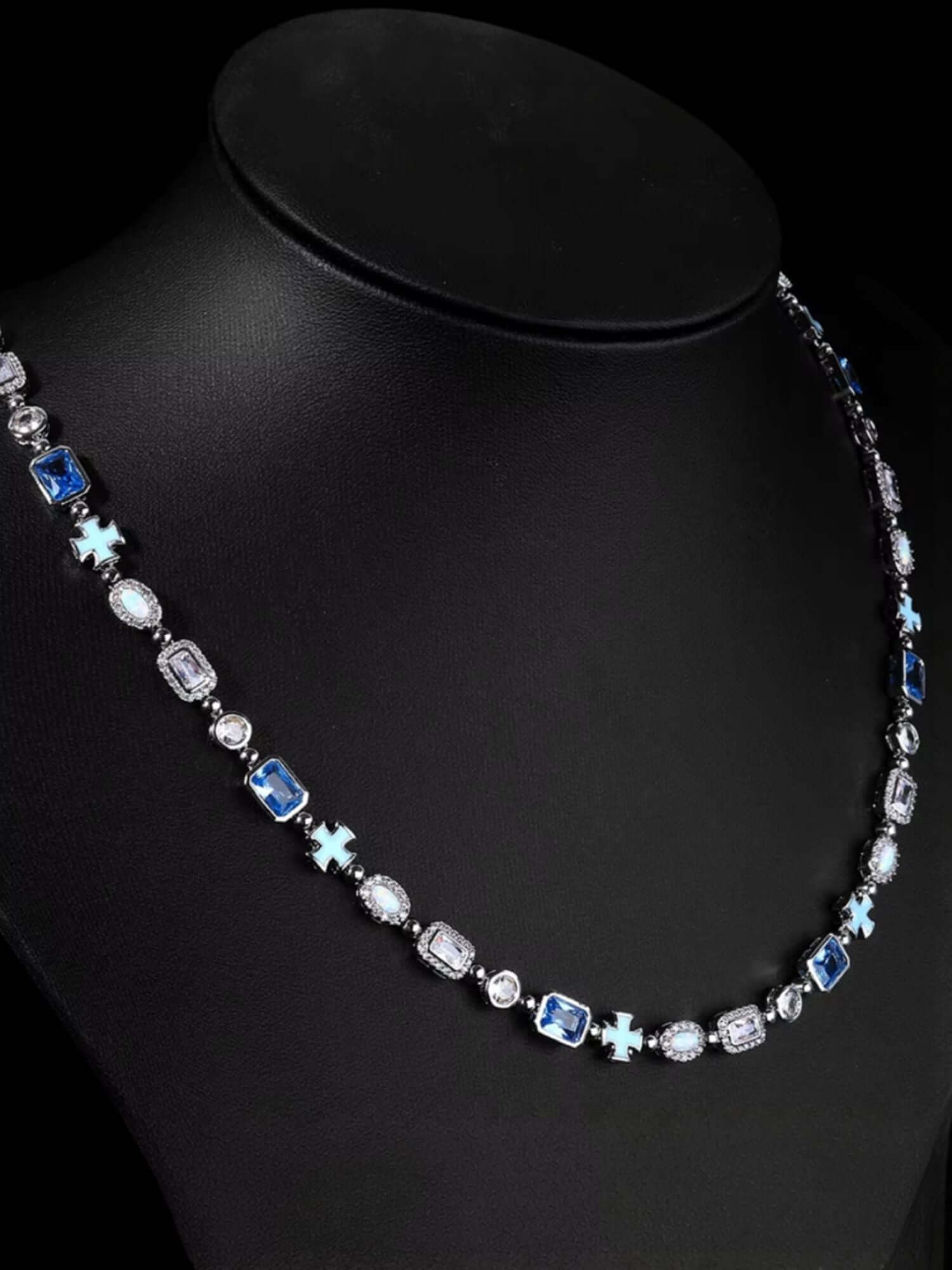 Kruis en Blauwe Edelstenen Ketting ICE Witgoud op een sieradendisplay met blauw en helder edelstenen.