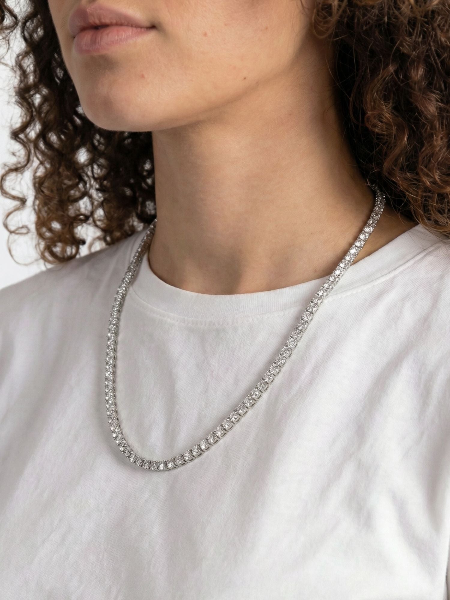 Vrouw met Zilveren tennis ketting van Carpe Ice op een witte t-shirt, met diamanten die luxe uitstralen.