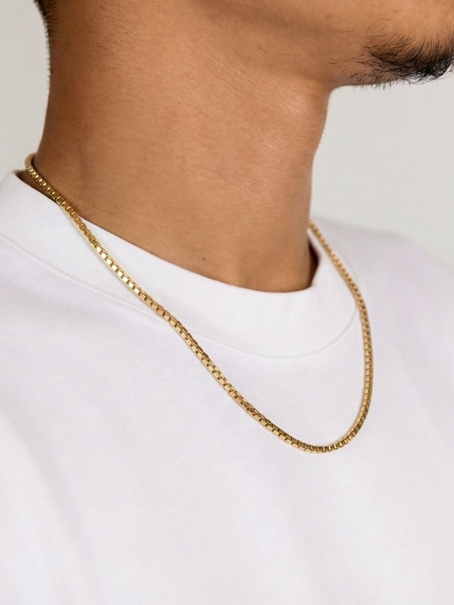 Close-up van een man die een gouden box ketting 2MM 3MM draagt op een wit T-shirt.