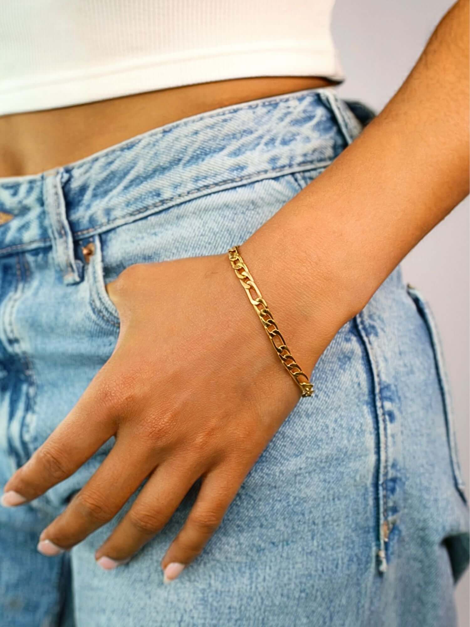 Gouden Figaro armband 3MM en 5MM gedragen op een hand, met een casual outfit van denim jeans.