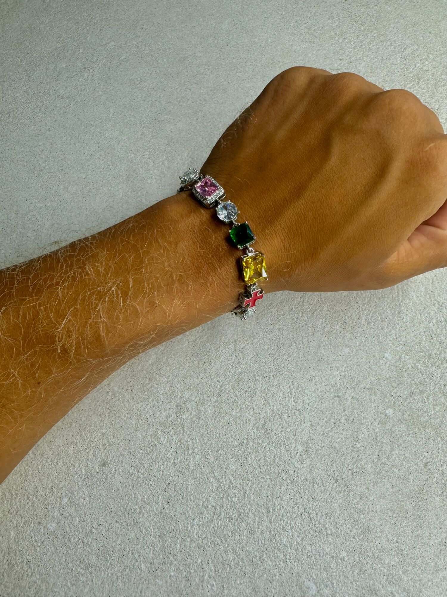 Kruis en edelstenen ICED OUT Witgoud Armband met kleurrijke edelstenen op een hand.