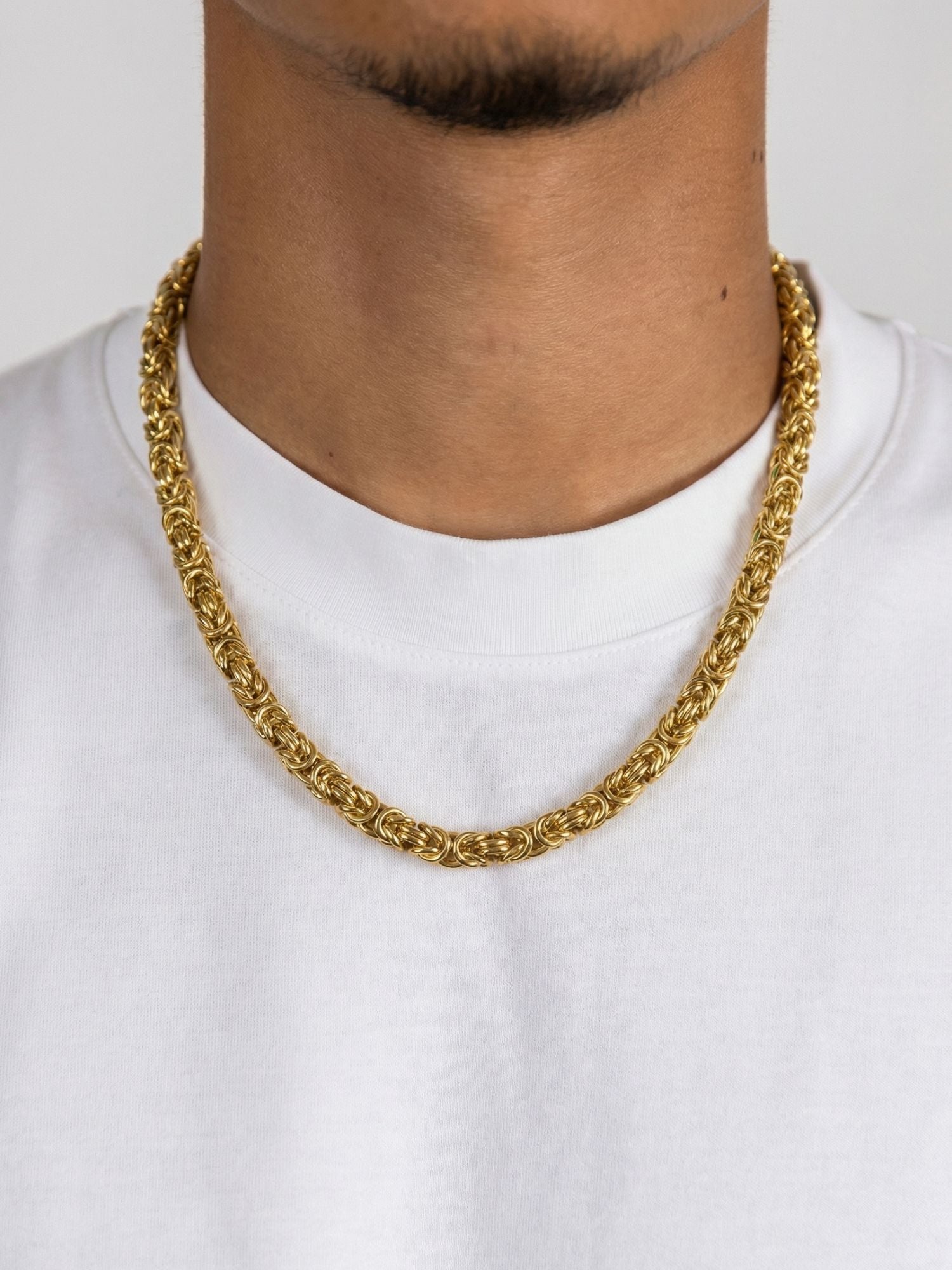 Gouden Byzantijnse Konings Ketting 6MM draperend over een witte trui, met een luxe en stijlvol ontwerp.