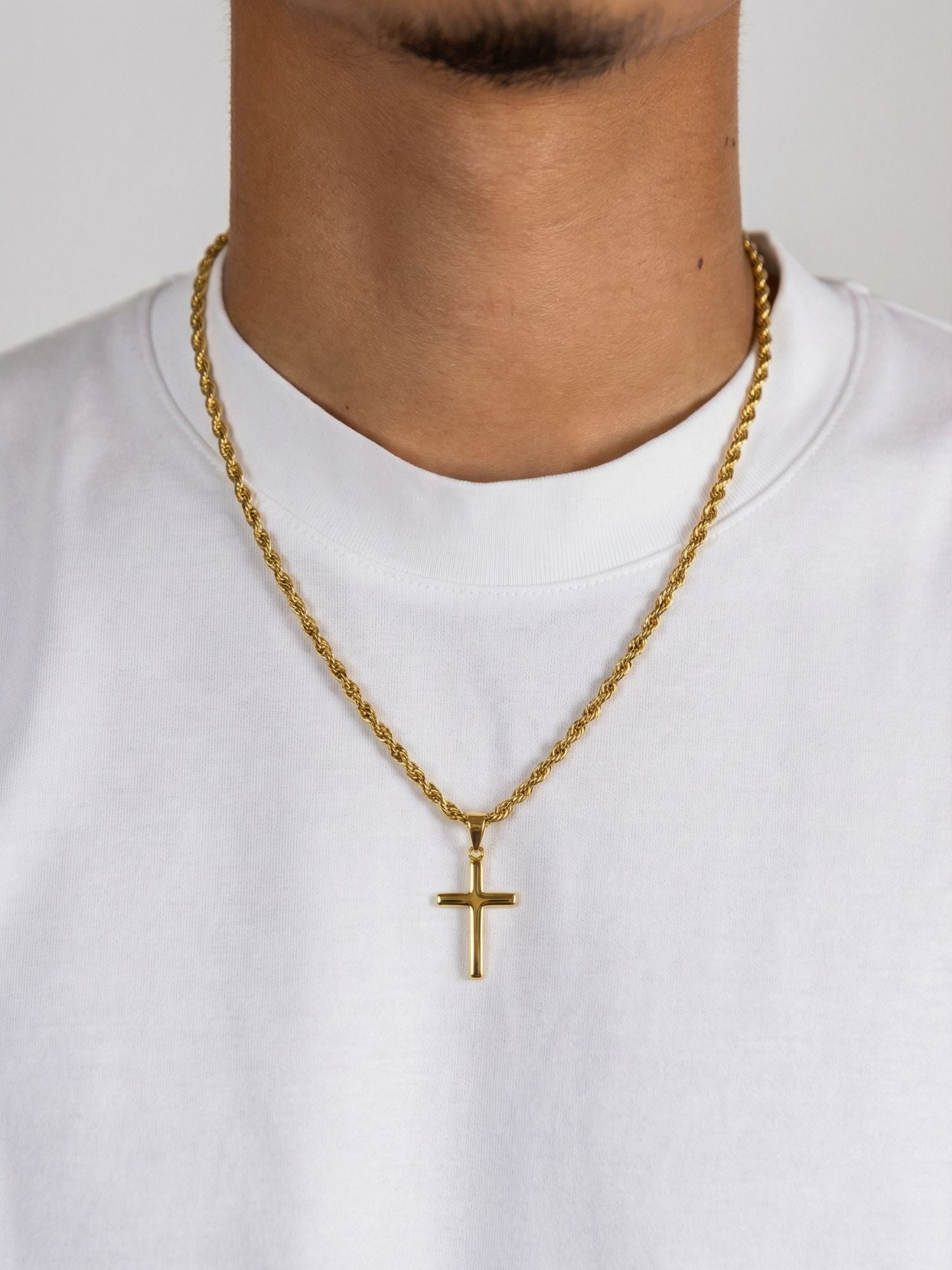 Gouden Luxe kruis hanger gedragen aan een gouden ketting over een witte shirt