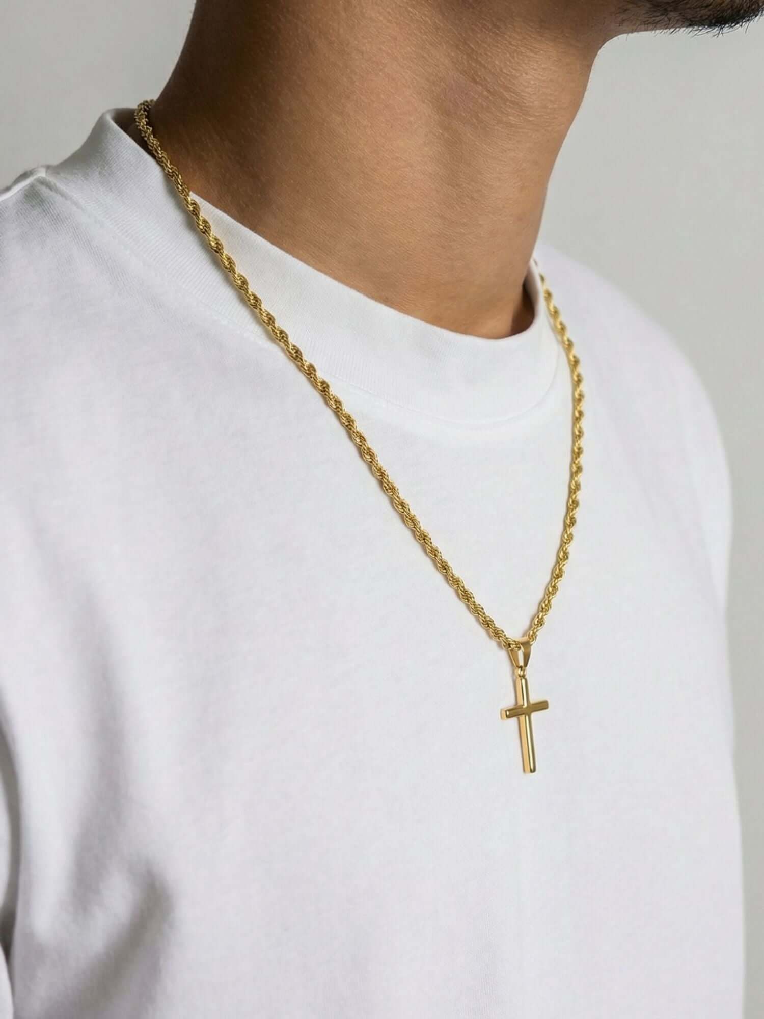 Ciondolo croce Luxe dorato indossato su una collana d'oro su una T-shirt bianca.