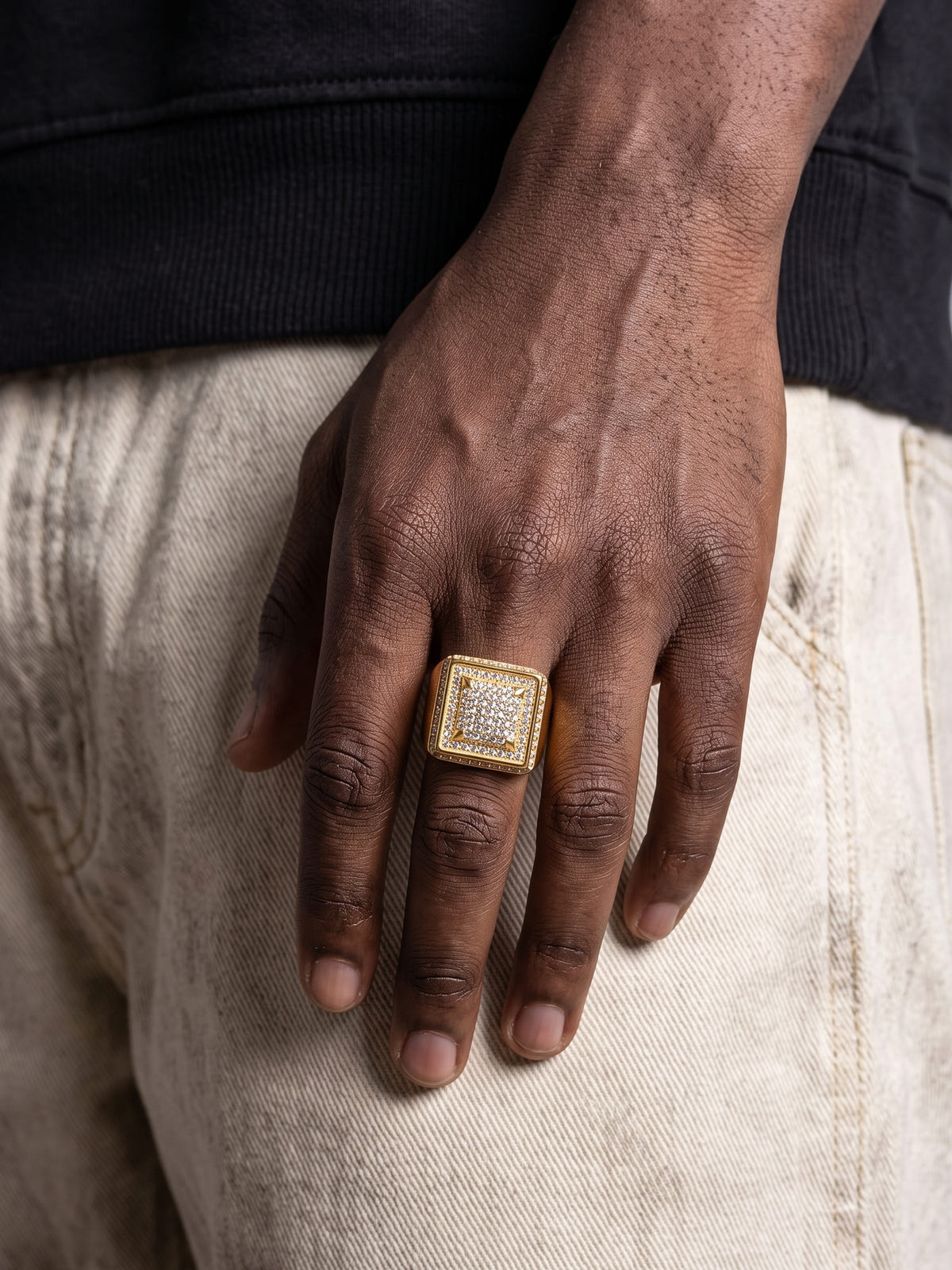 Nahaufnahme des Ice Blox Rings goldfarben Iced Out mit quadratischem, gestuftem Kopf voller Steine am Finger eines Mannes