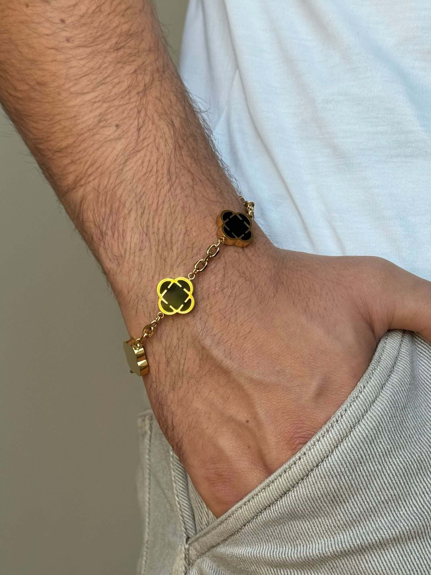 Bracciale a trifoglio dorato con pietra di onice nera indossato al polso da uomo, bracciale con quadrifoglio dorato e pietra di onice nera