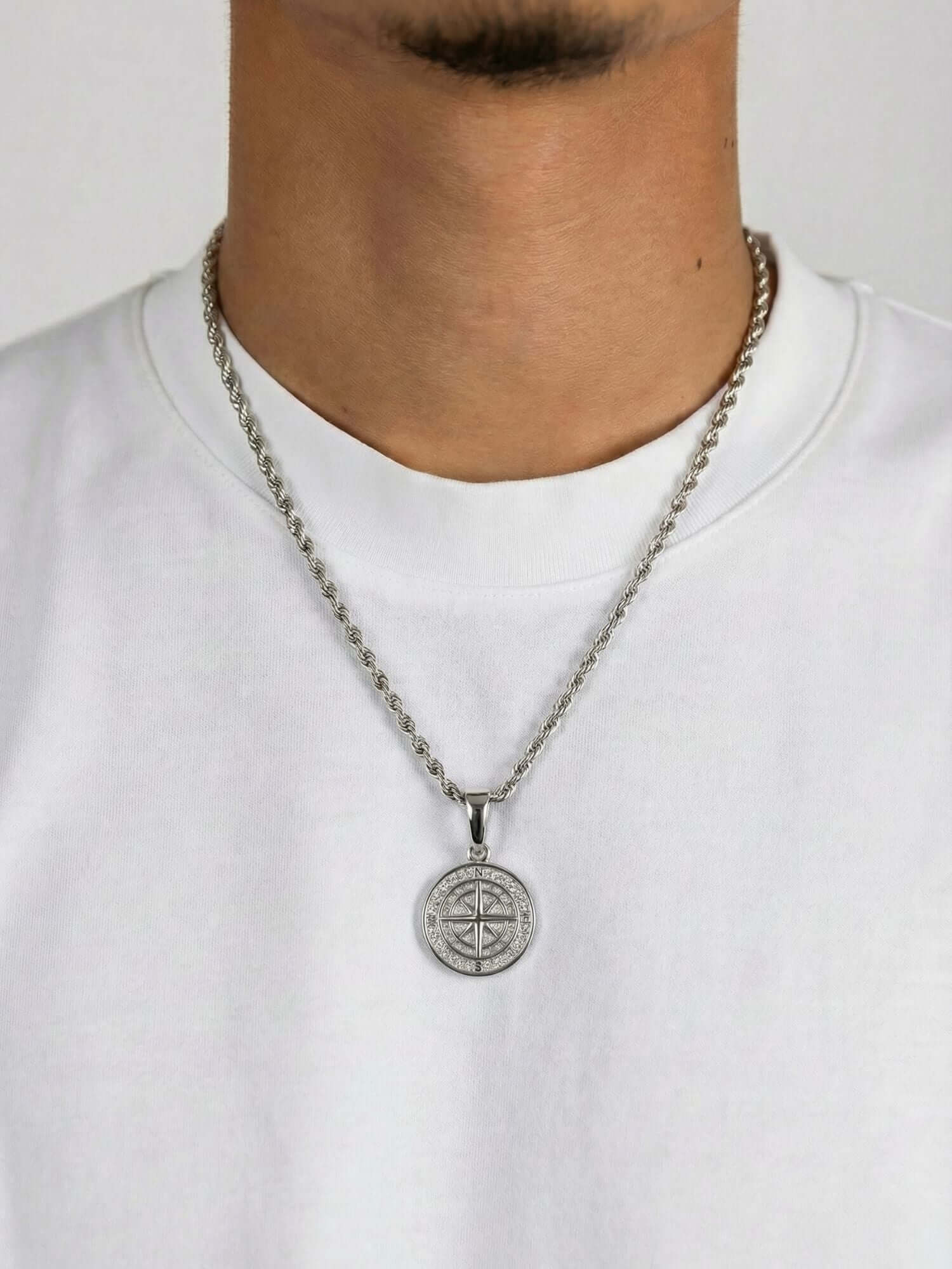 Kompasshänge i silver på kedja, bärs av en modell i en vit T-shirt.