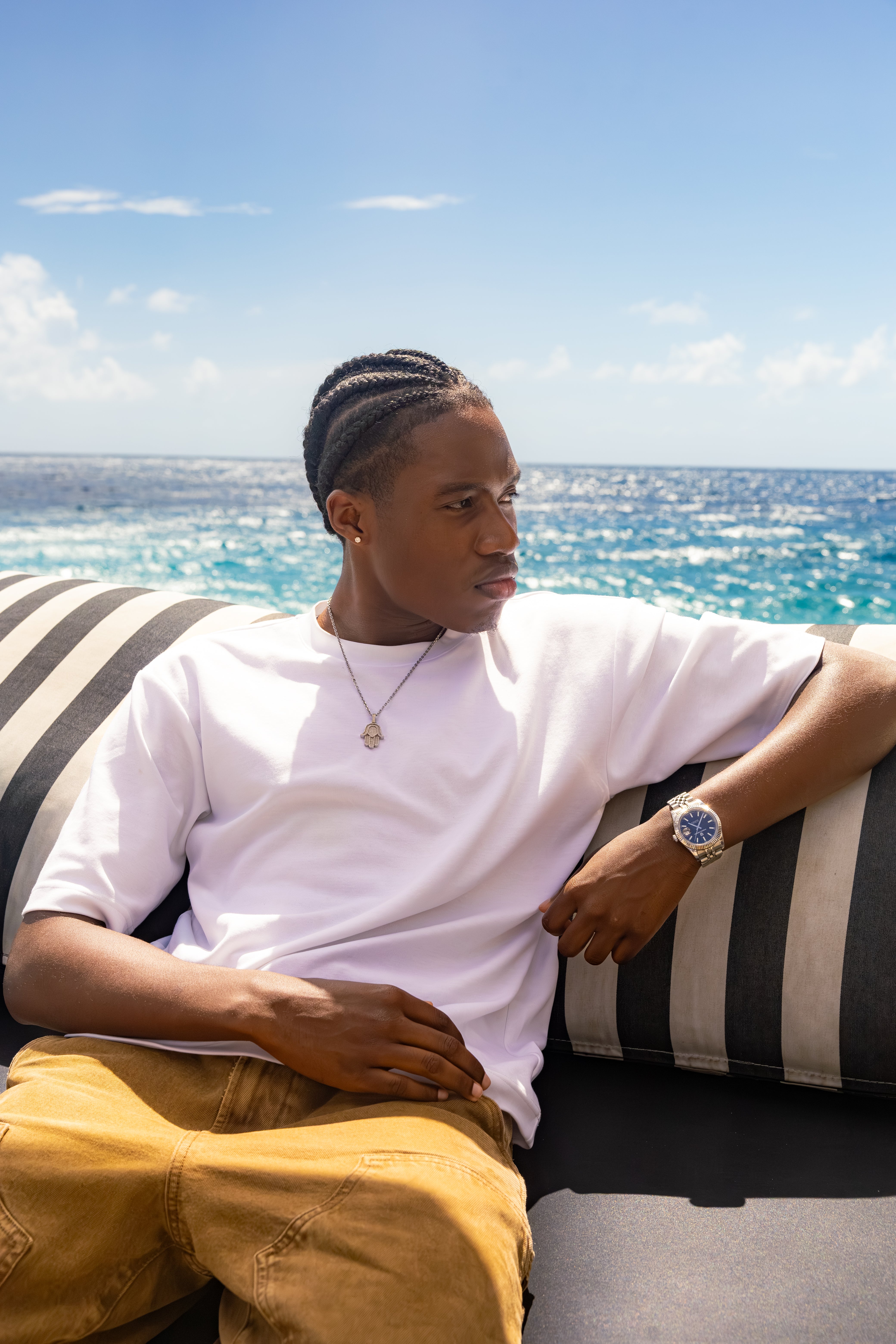 Man met cornrows in wit T-shirt ontspant op gestreepte loungebank aan zee op zonnige dag