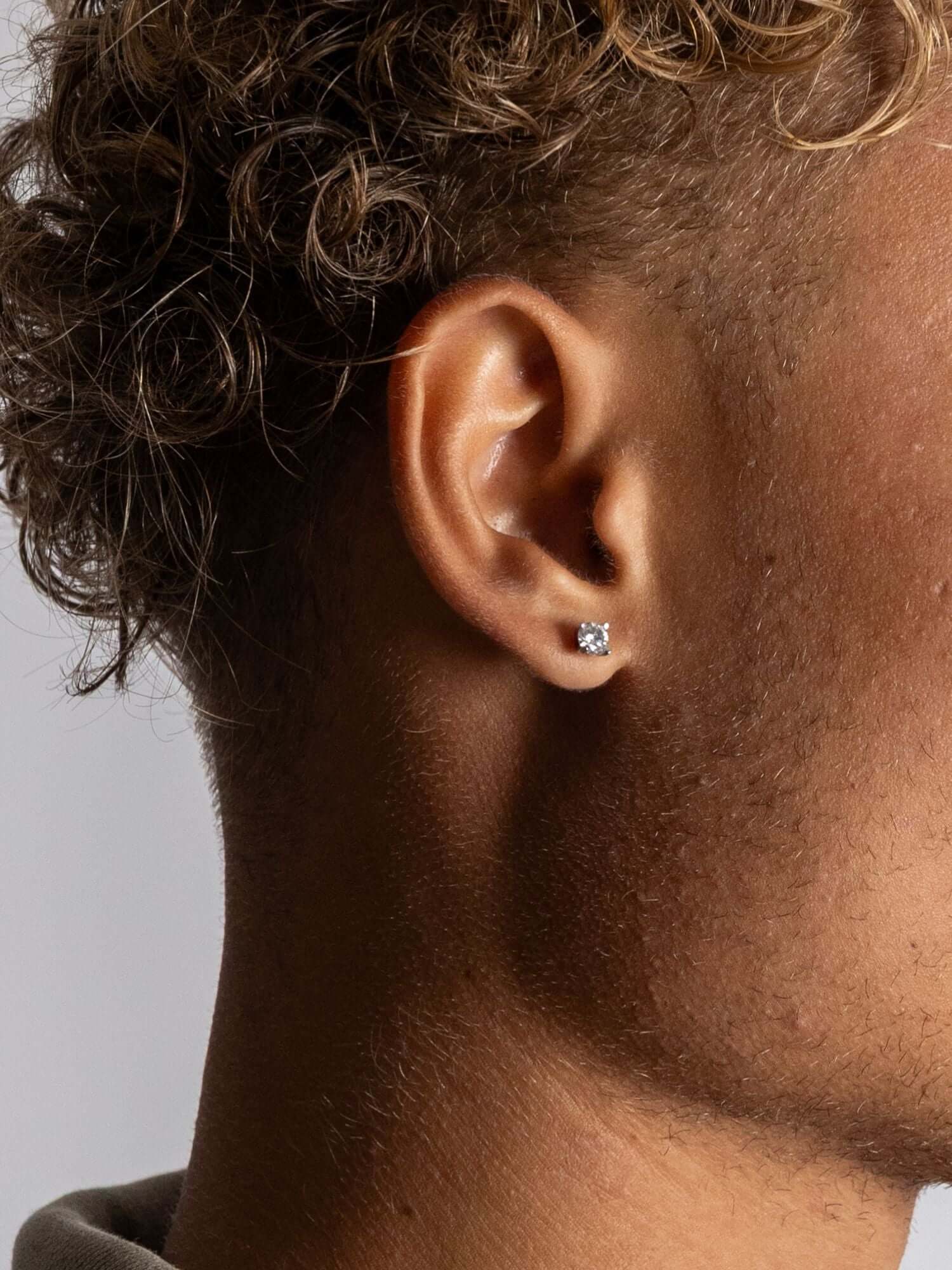 Diamanten Oorbellen Moissanite 5MM zichtbaar in het oor van een man met krullend haar.