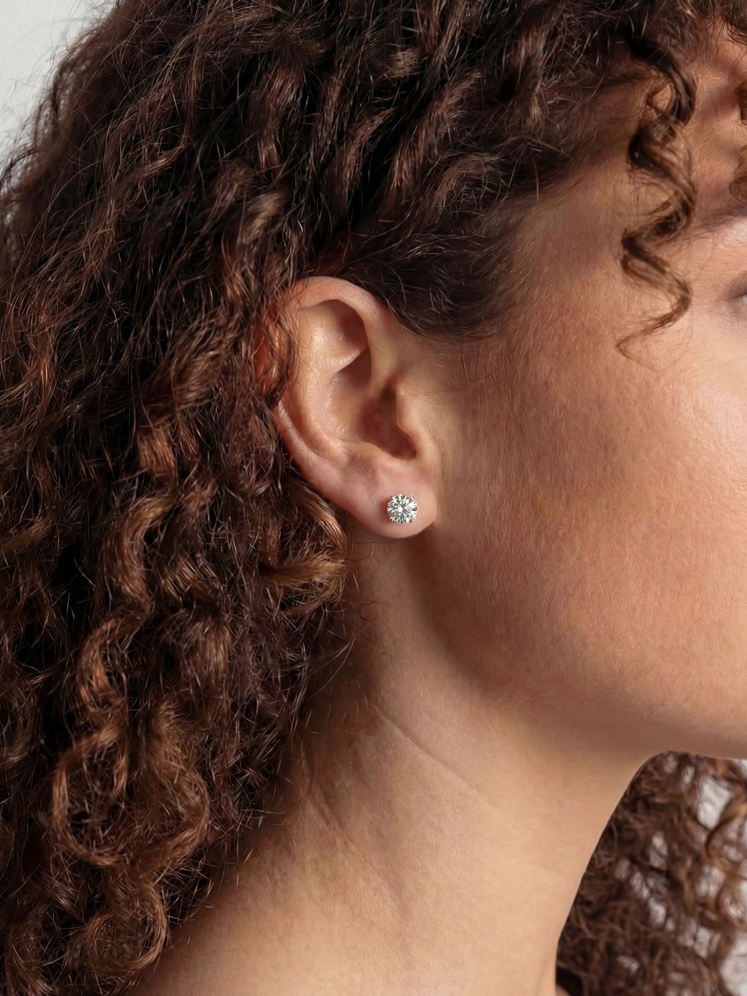 Diamanten Oorbellen MOISSANITE Witgoud 5MM in het oor van een model met krullend haar.