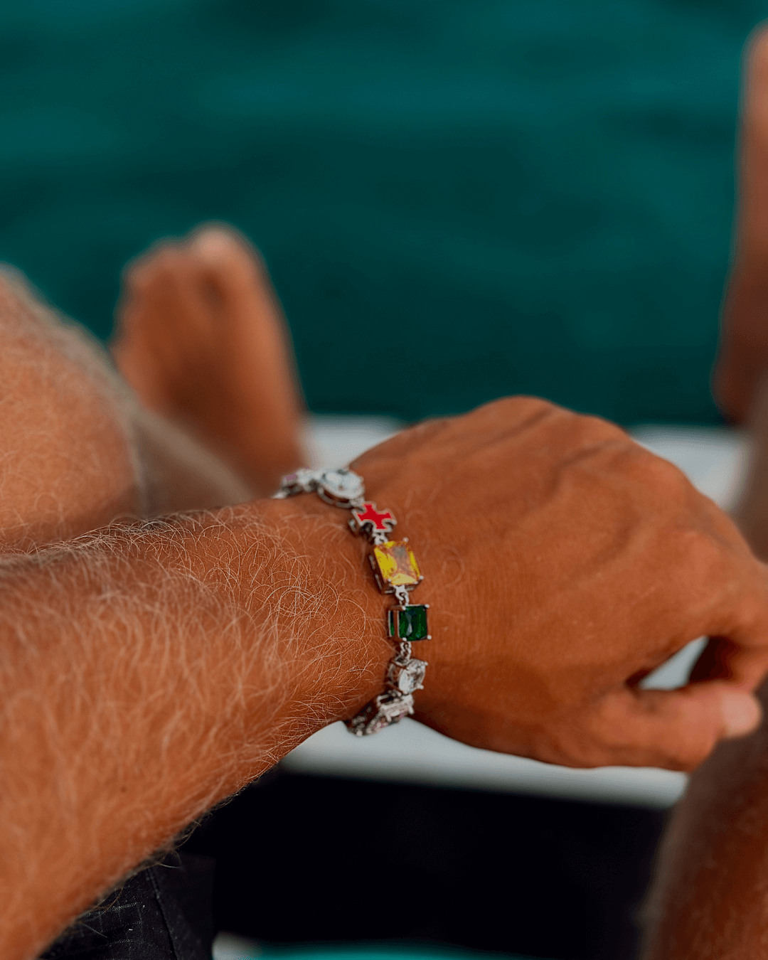 Kruis en edelstenen ICED OUT Witgoud armband met kleurrijke edelstenen, gedragen op een pols.