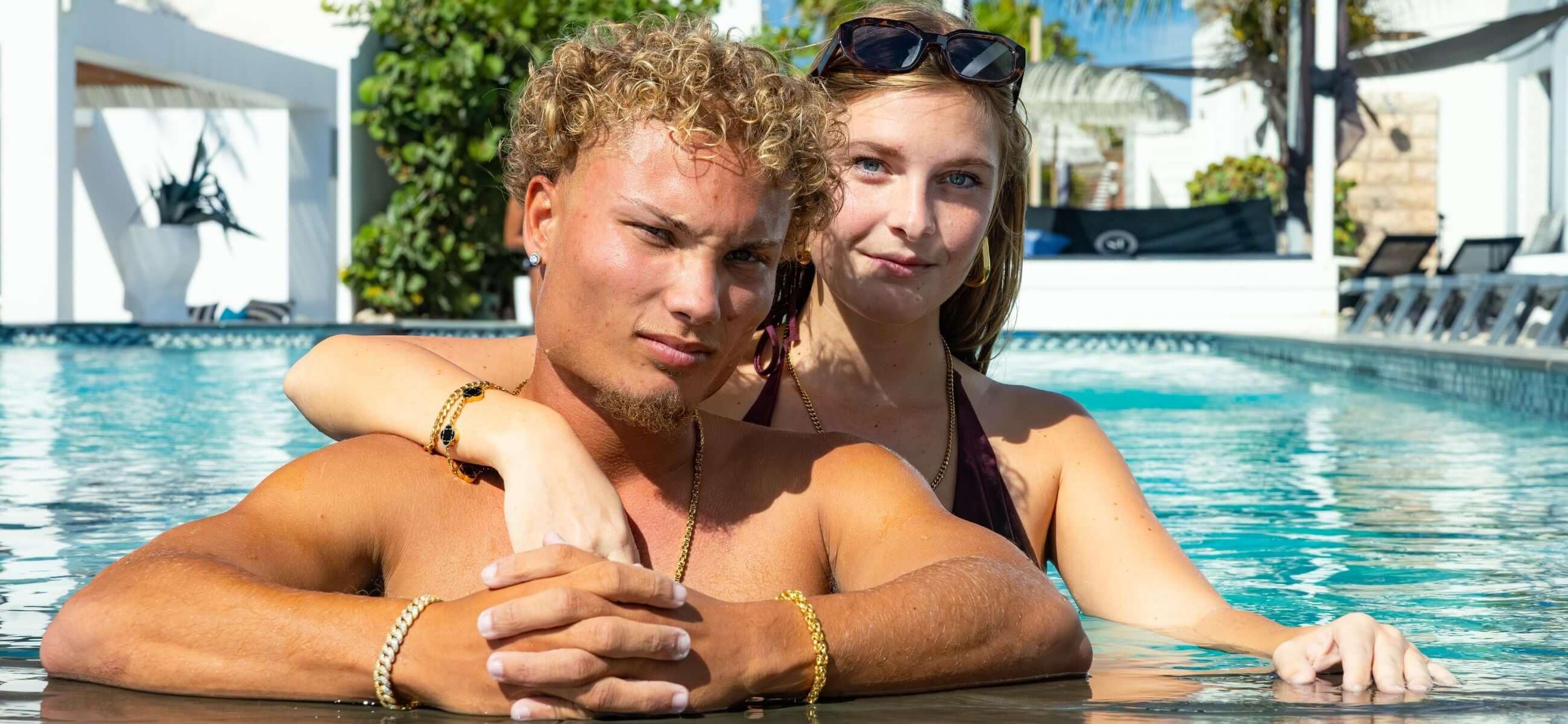 Koppel bij zwembad draagt Carpe Ice gouden ketting en armbanden, luxe sieraden