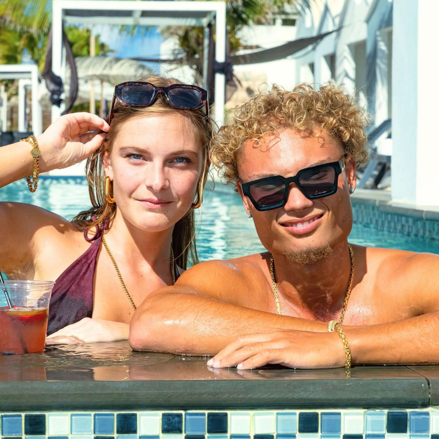 Twee vrienden ontspannen in een zonnig zwembad met zonnebril, cocktail en tropische vakantiesfeer