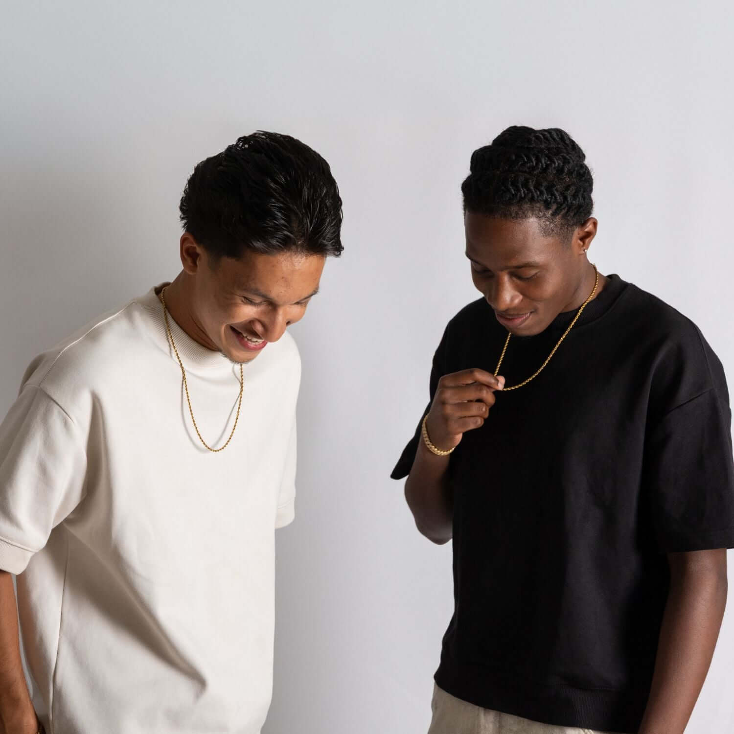 Twee mannen dragen minimalistische gouden kettingen bij casual T-shirts, moderne sieradenstijl in studio