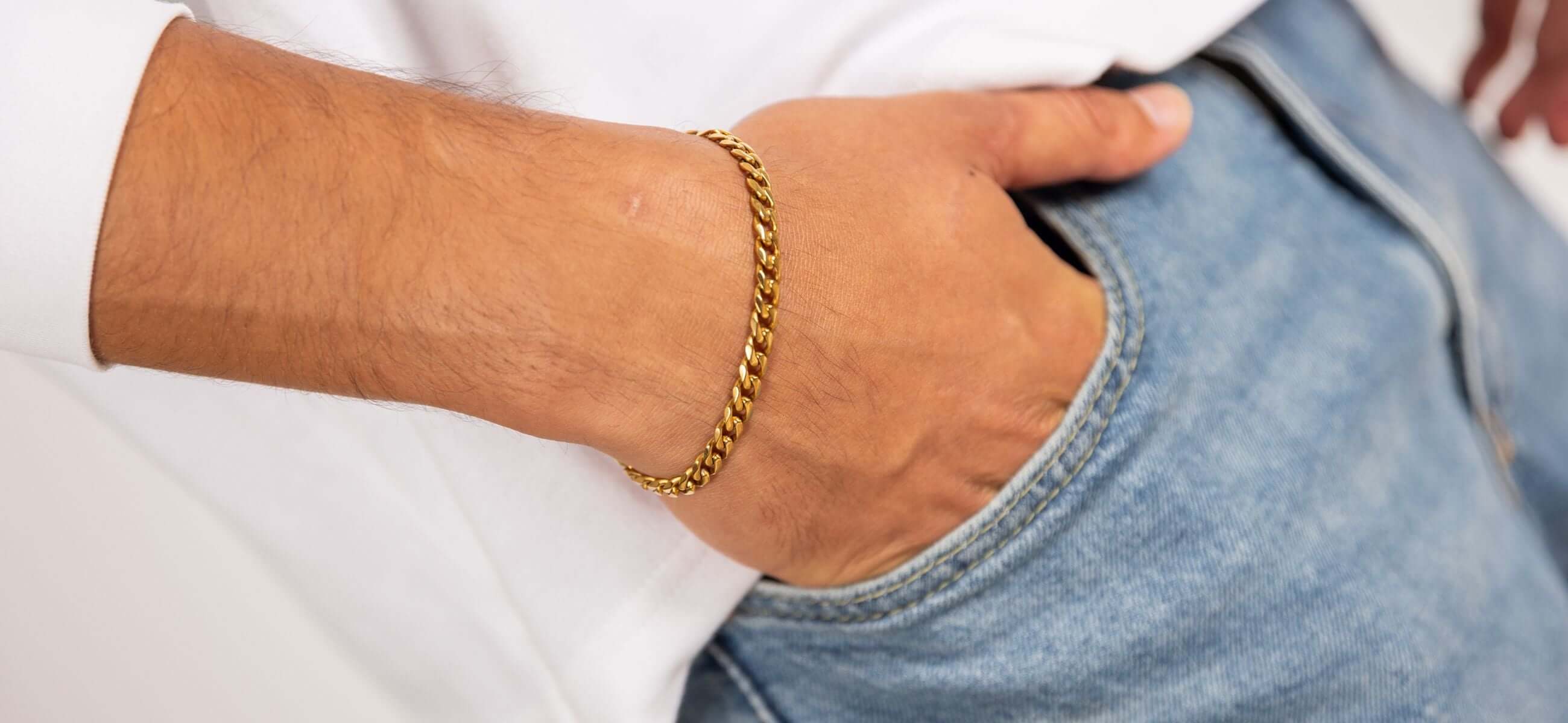 Close-up van een hand met gouden schakelarmband in de zak van een lichte spijkerbroek, casual herenaccessoire
