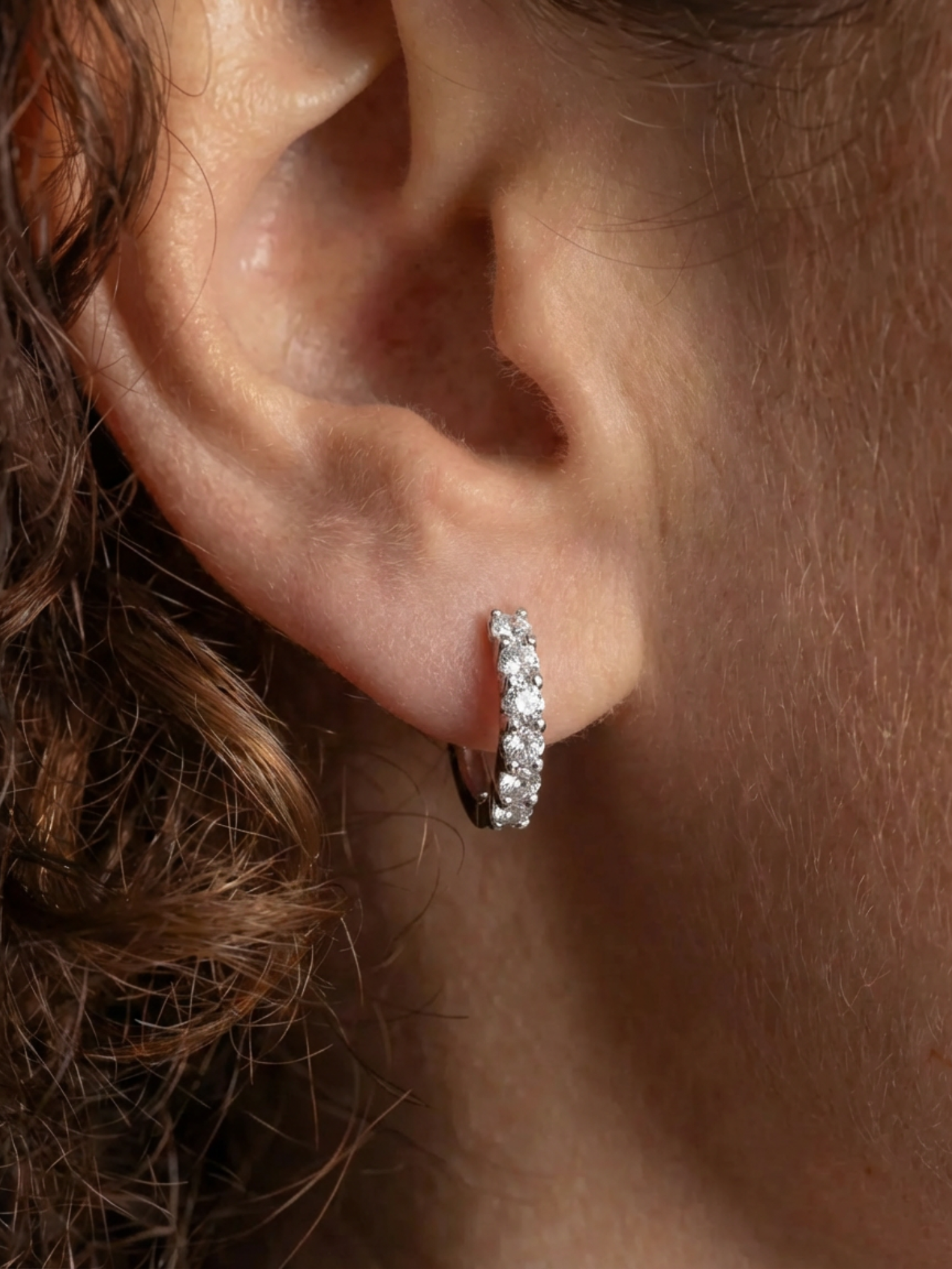 MOISSANITE HOOP DIAMOND OORBELLEN WITGOUD in zilveren kleur, dicht bij het oor van een persoon met krullend haar.