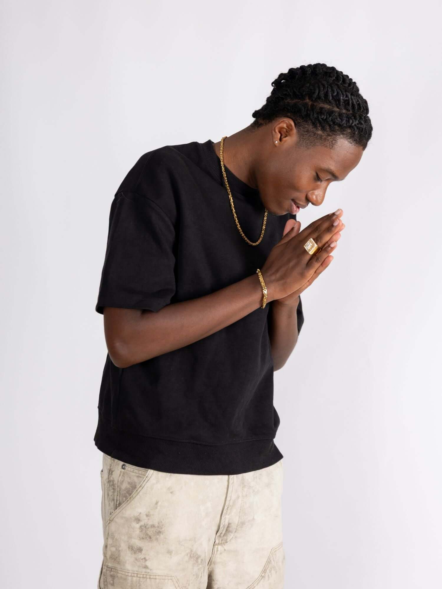 Man wearing a black shirt and gold accessories, including a konings schakel armband, looking down in a thoughtful pose.