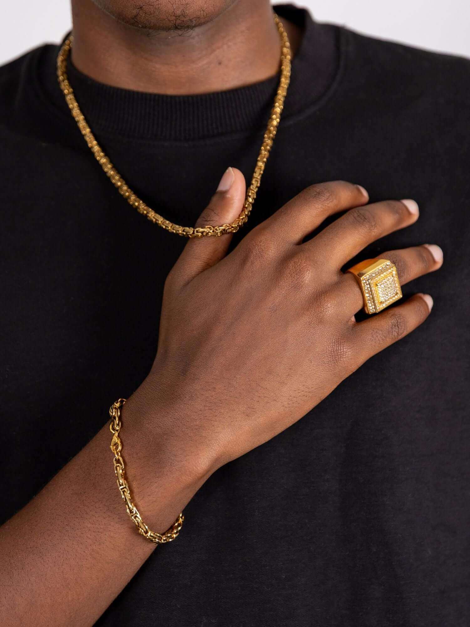 Man wearing a konings schakel armband in gold, showcasing luxury jewelry style with matching ring and chain.