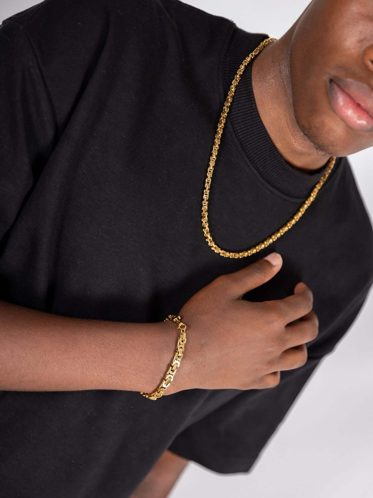 Gouden konings schakel ketting 3MM gedragen door een man met een zwart shirt, accessorized met een gouden armband.