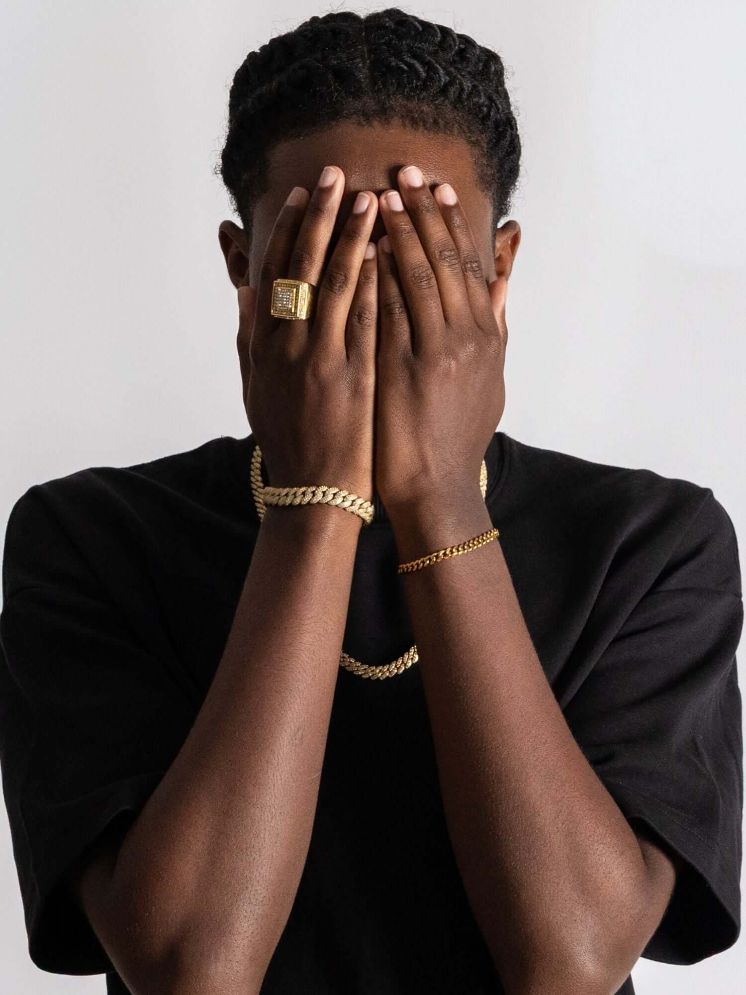 Cuban link armband goud worn by a person covering their face with hands, showcasing luxury jewelry.