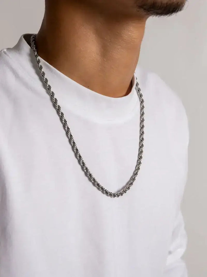 Een man draagt een trendy rope sieraden ketting over een witte trui, perfect voor elke gelegenheid.