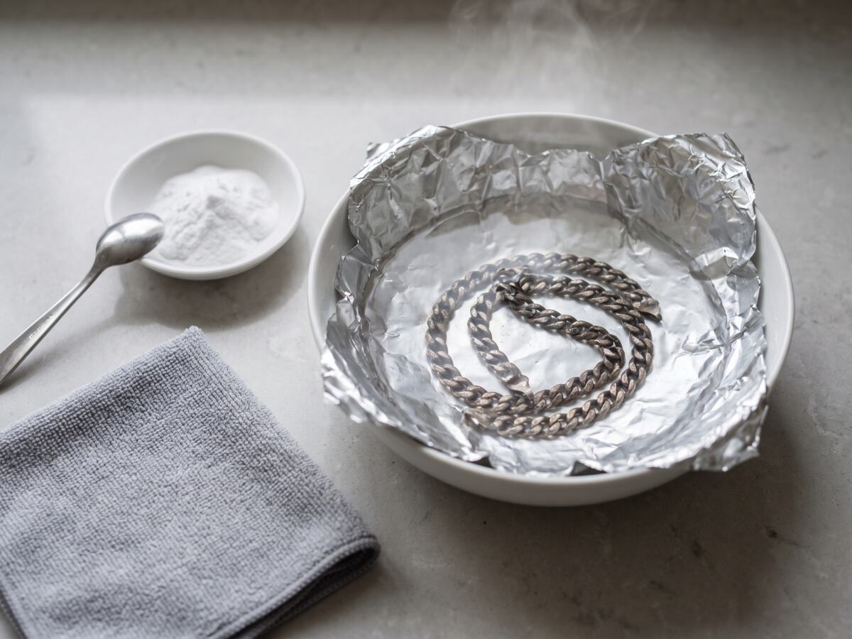 Schaal bekleed met aluminiumfolie met een aangeslagen zilveren schakelketting erin, baksoda en poetsdoek ernaast