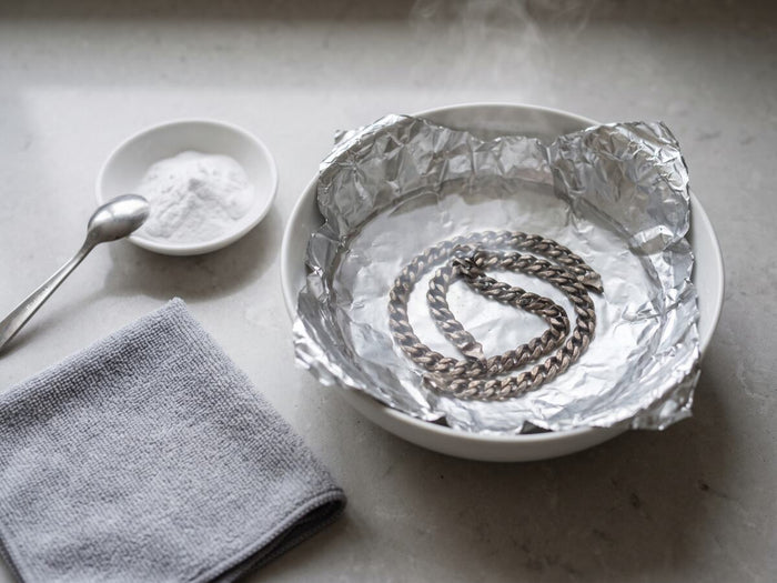 Schaal bekleed met aluminiumfolie met een aangeslagen zilveren schakelketting erin, baksoda en poetsdoek ernaast