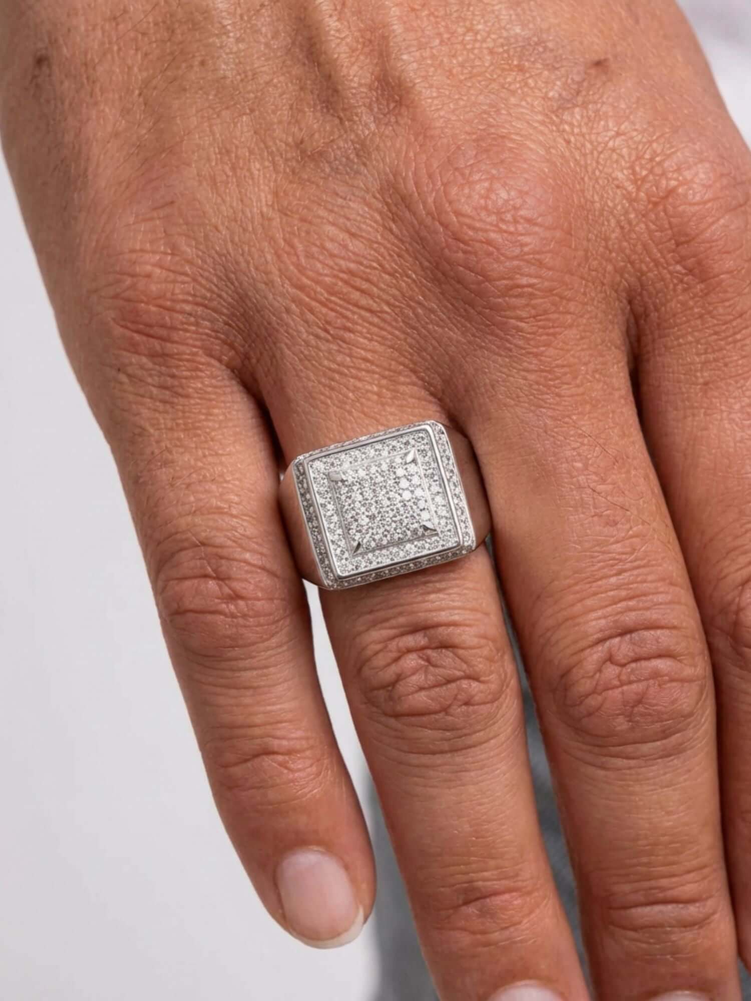 Mano con anillo caja ICED OUT de plata con impresionantes diamantes simulados, que muestra su diseño lujoso.