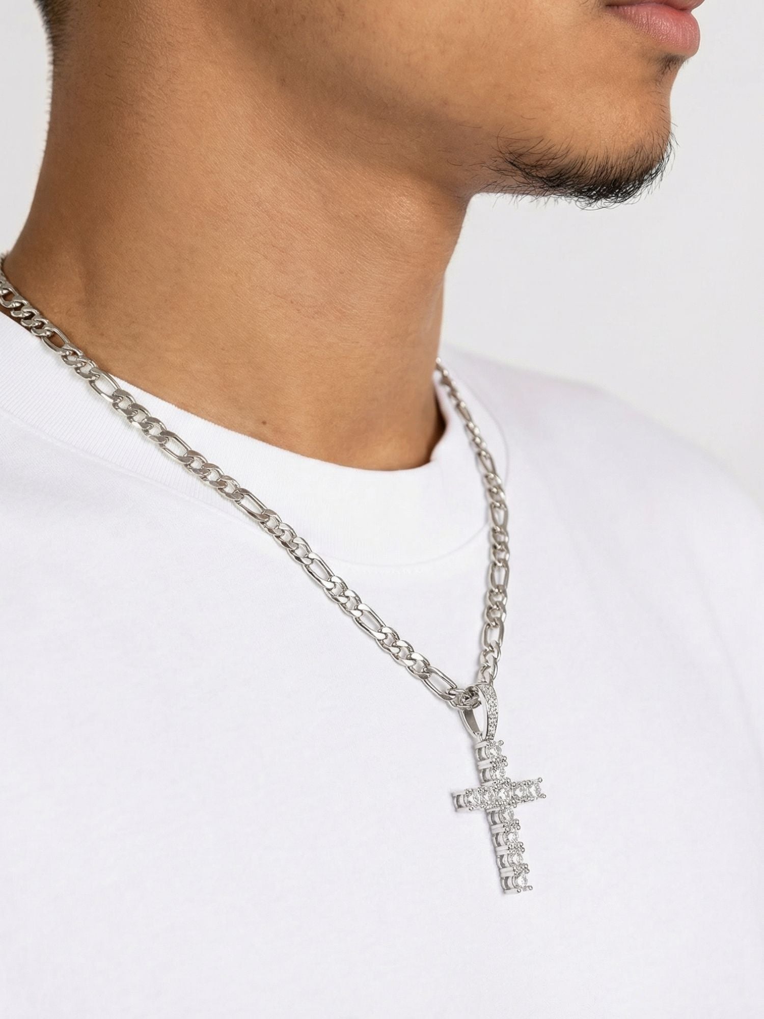 Zilveren kruis hanger met ICED OUT uitstraling, gedragen aan een zilveren ketting op een witte t-shirt.