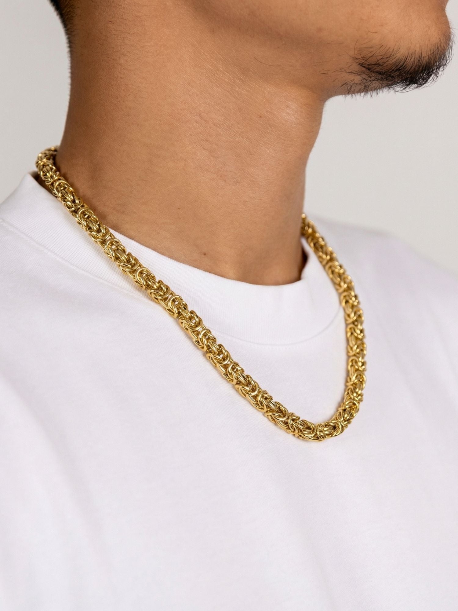 Gouden Byzantijnse Konings Ketting 6MM draagbaar op een witte t-shirt, stralend in luxe gouden afwerking.