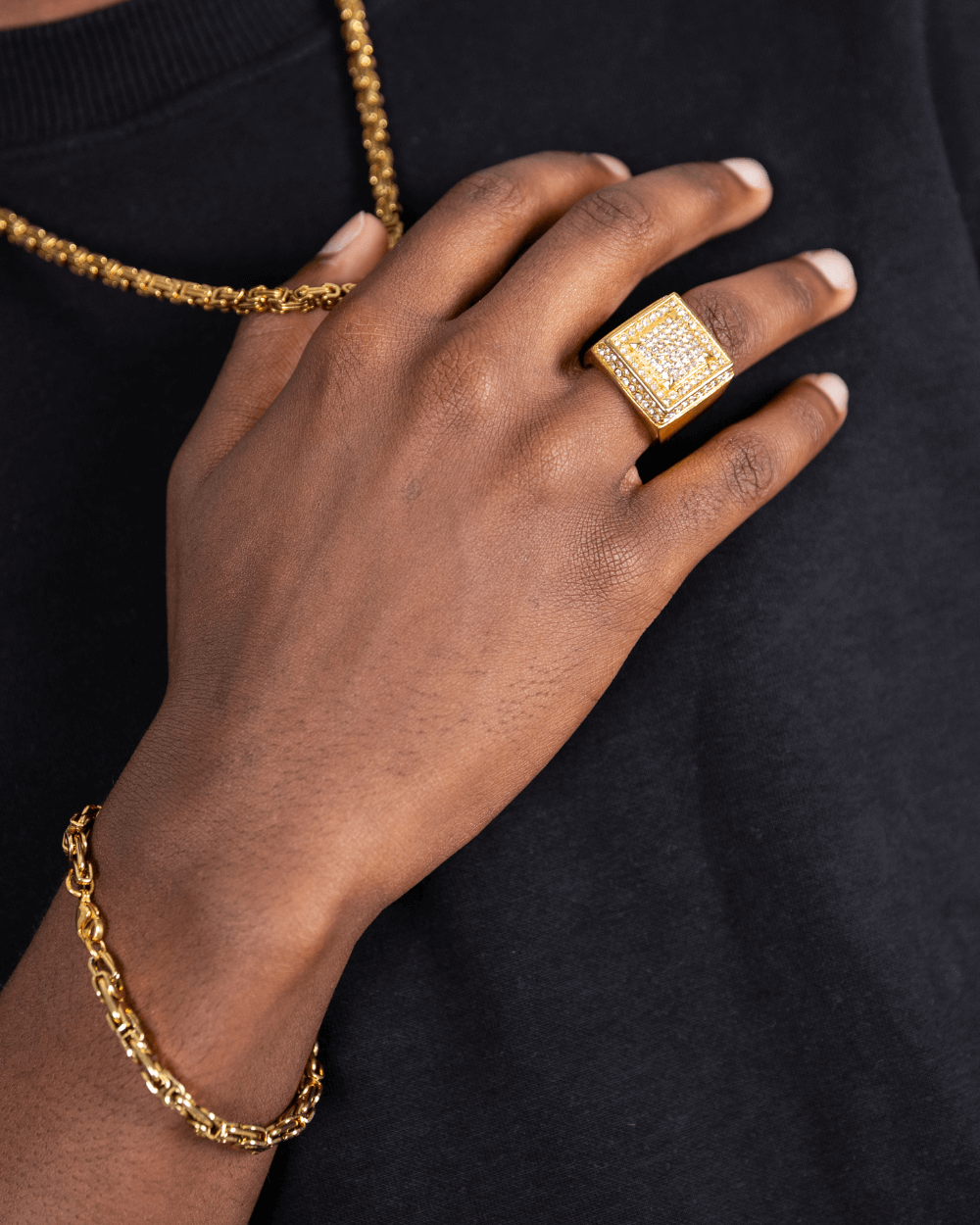 Anello Ice Blox in oro indossato alla mano, che mostra il suo design iced out e il gioiello in oro con catena e bracciale.