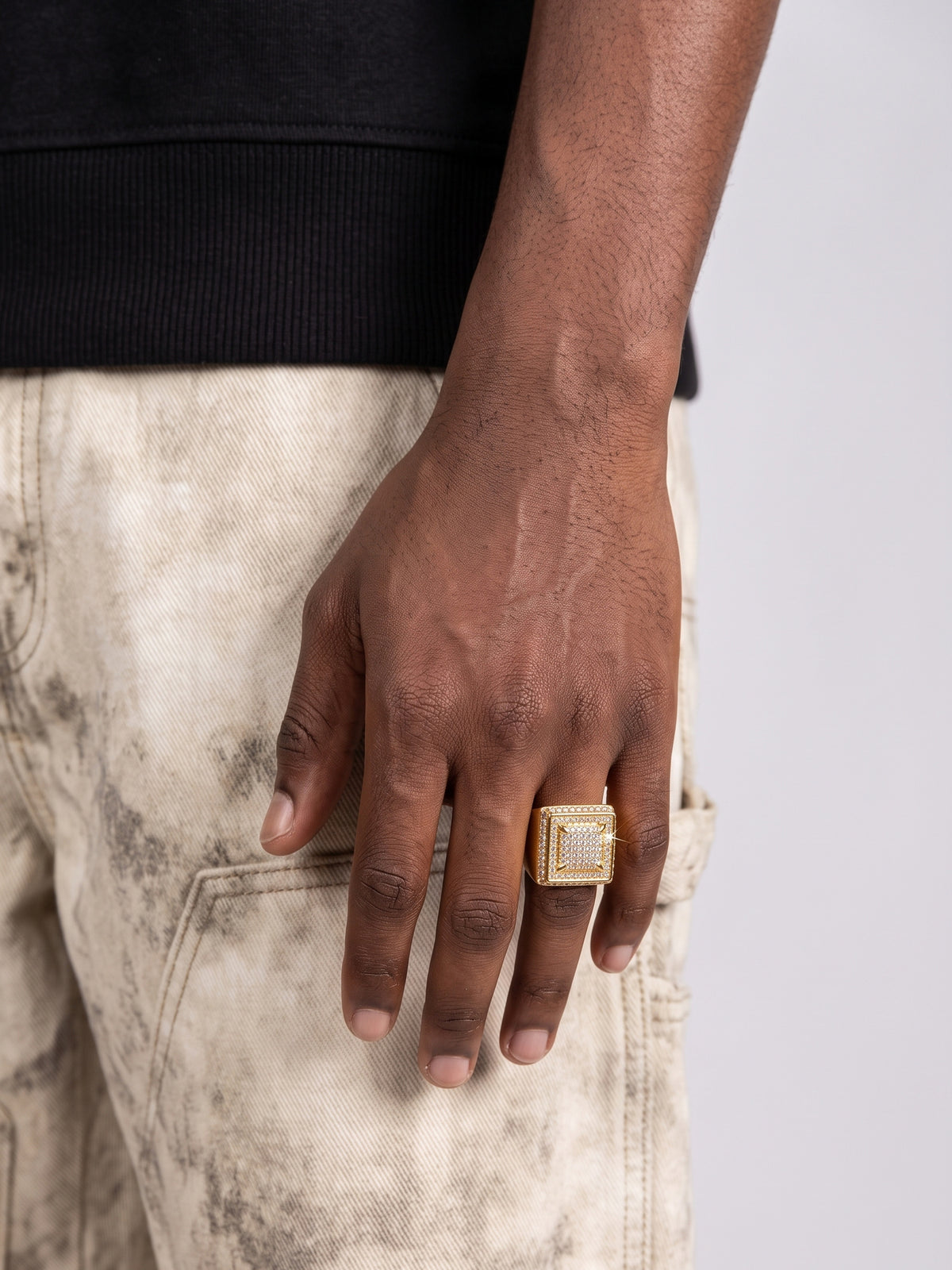 Ice Blox Ring Goud iced out om de middelvinger van een ontspannen hand naast een lichte broek en zwarte sweater.
