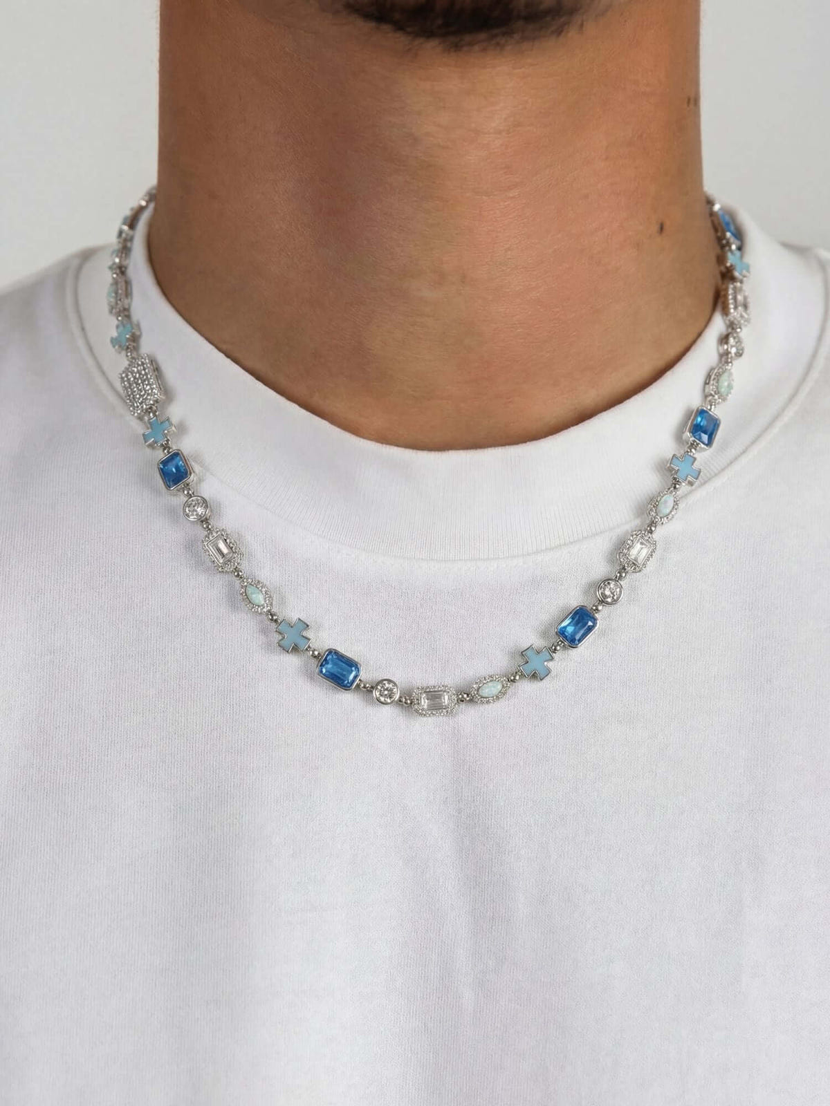 Kruis en Blauwe Edelstenen Ketting ICE Witgoud gedragen door man, elegante uitstraling met blauwe edelstenen.