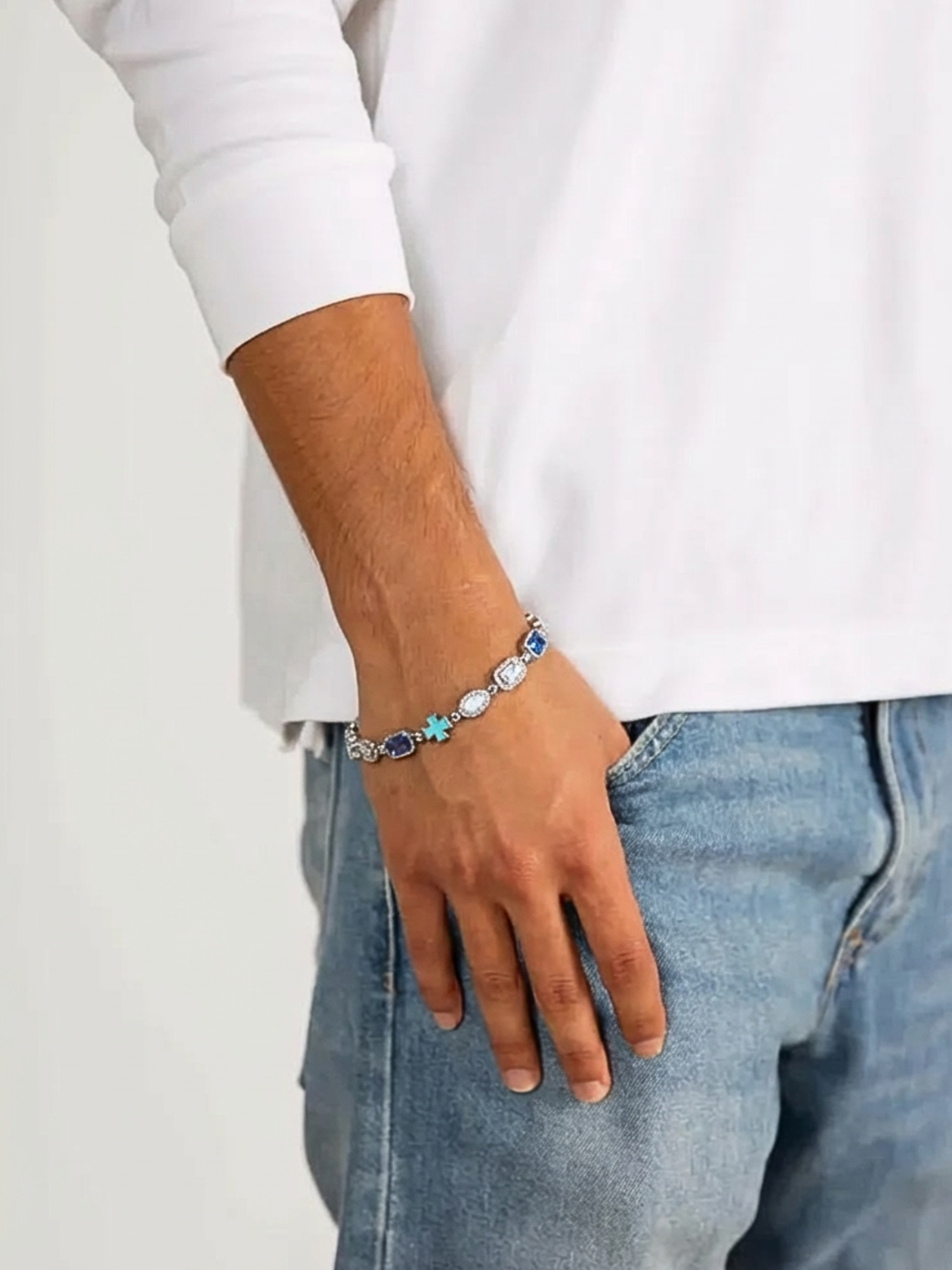 Kruis en Blauwe Edelstenen Armband ICE Witgoud gedragen door een man met een witte trui en jeans.