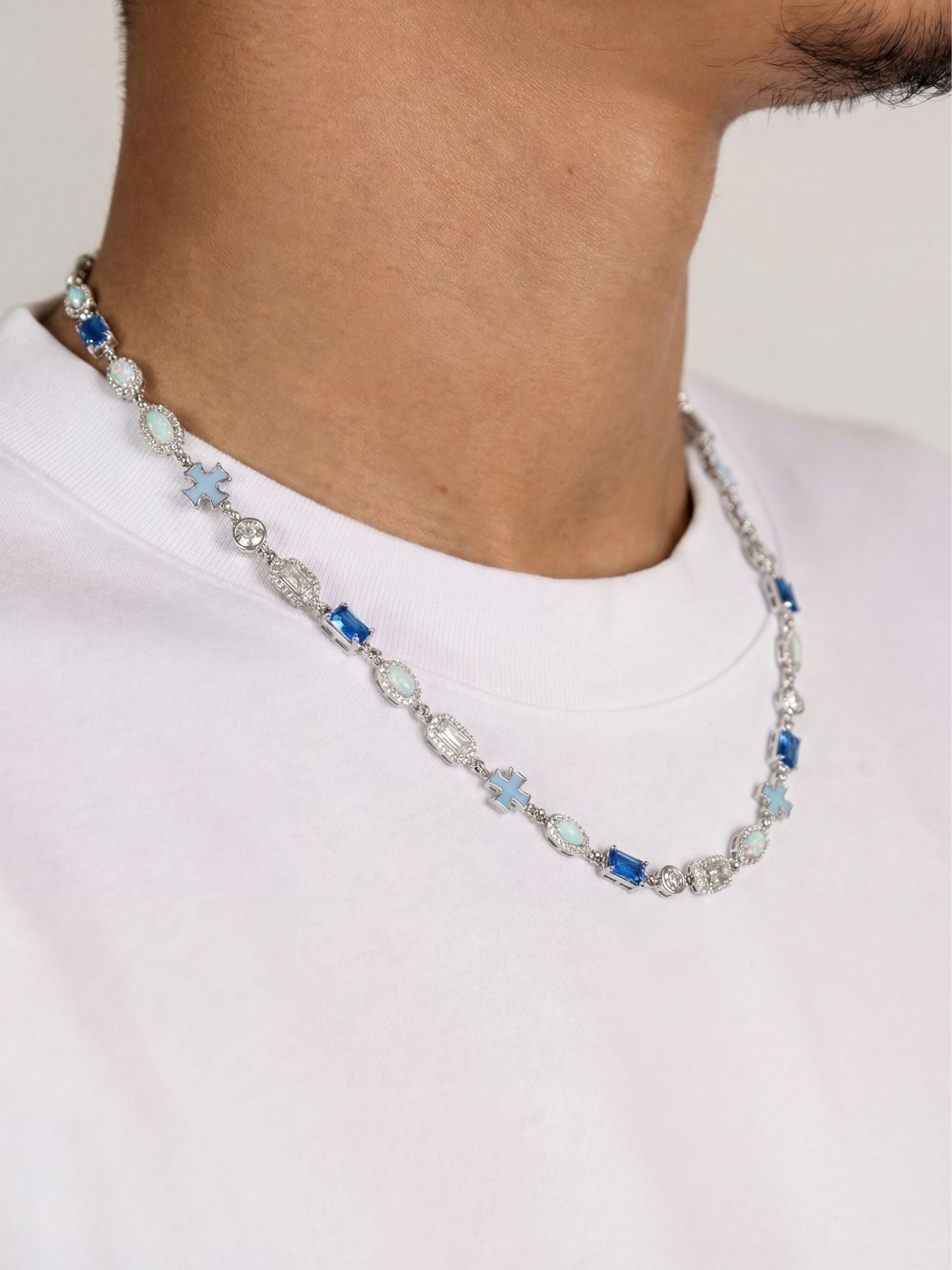 Kruis en Blauwe Edelstenen Ketting ICE Witgoud te zien op een mannelijke model in een witte T-shirt.