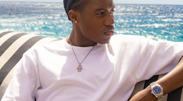 Man in wit T-shirt ontspant op boot met zee op de achtergrond, draagt polshorloge en ketting